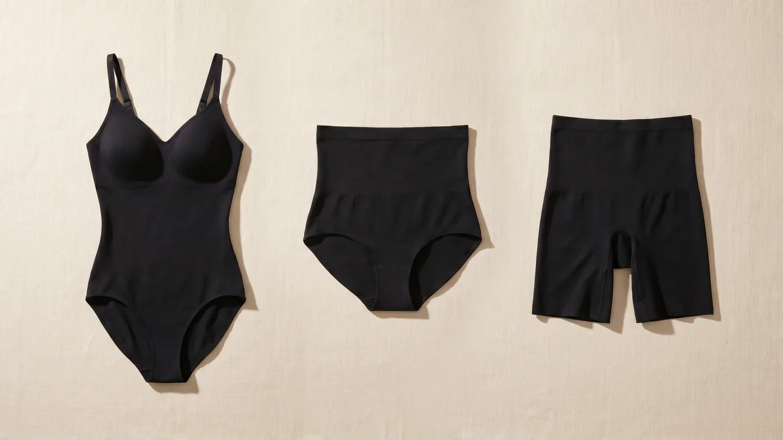 Trois pièces shapewear Elya noir flatlay : body gainant, culotte gainante, shorty gainant sur fond beige