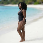 Maillot sculptant Elya noir vue de profil — silhouette galbée et taille affinée sur plage